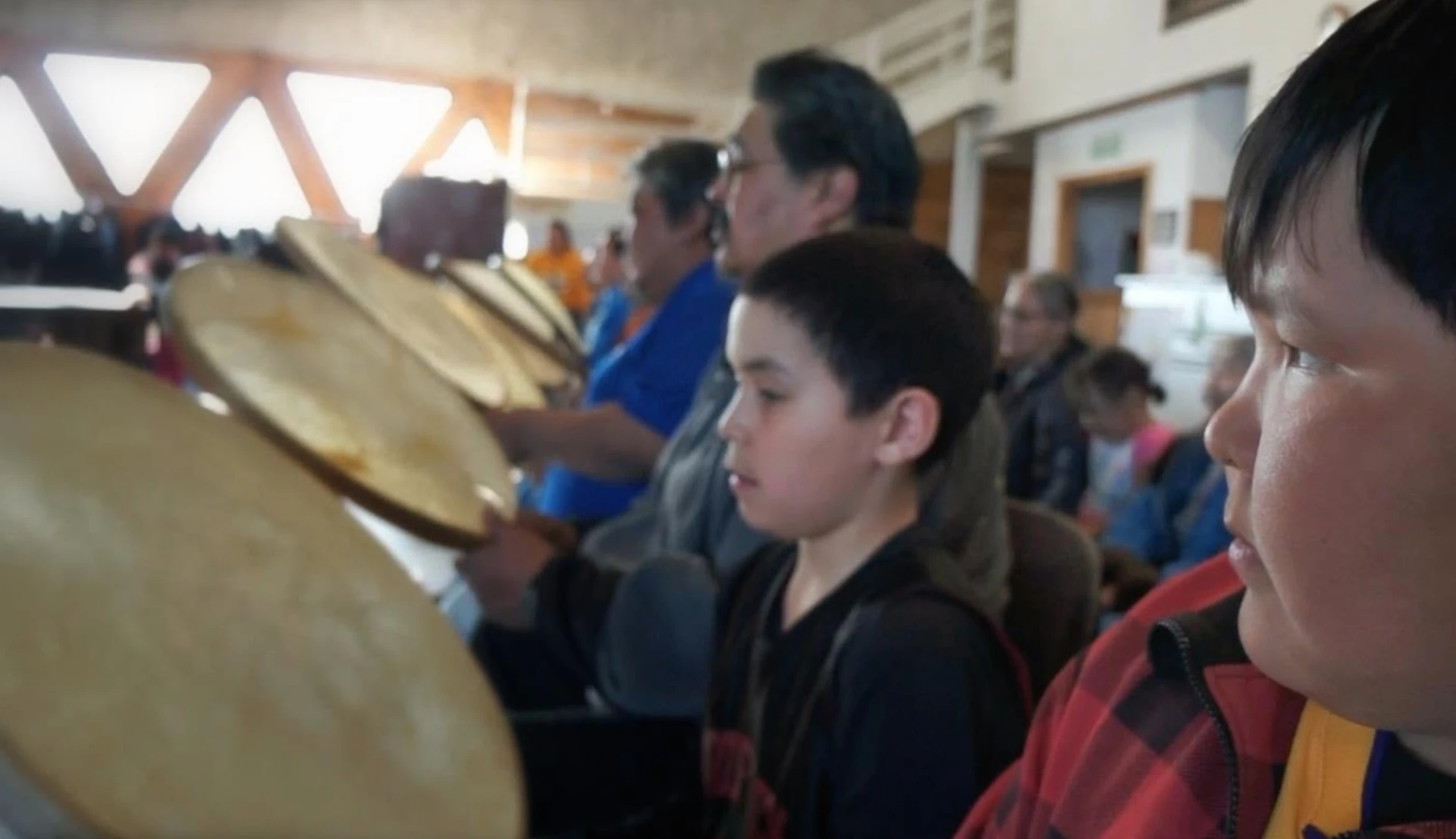 A row of Iñupiaq drummers holding qiḷaun hand drums during a community gathering